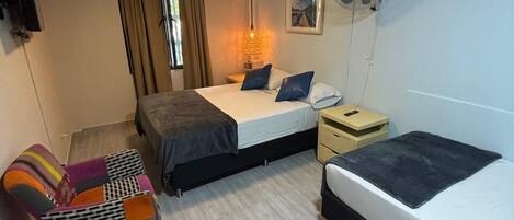 Una habitación de hotel compacta con dos camas, un sofá, un televisor, un ventilador y una ventana con cortinas.