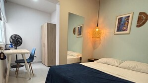 Un dormitorio con una cama, un escritorio, una silla y un ventilador.