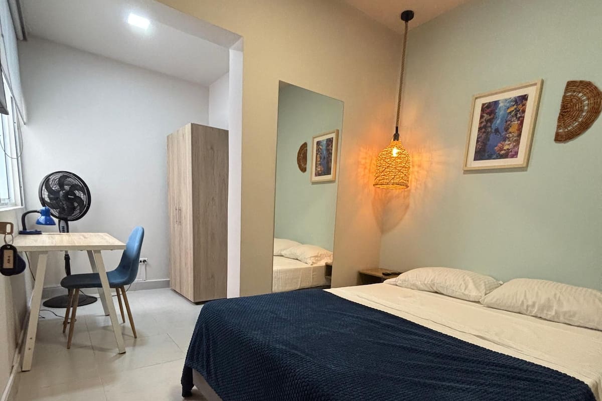 A bedroom with a bed, a desk, a chair, and a fan.