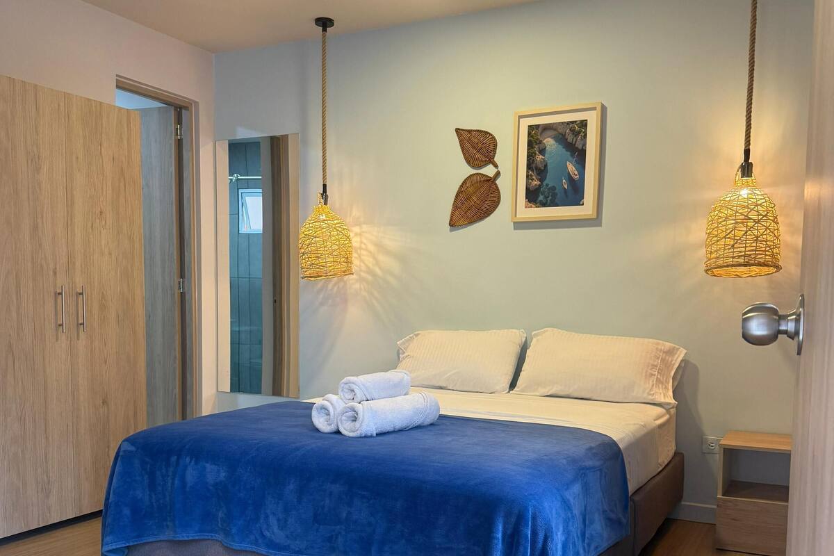 A modern bedroom with a bed, wooden wardrobe, and two hanging light fixtures.