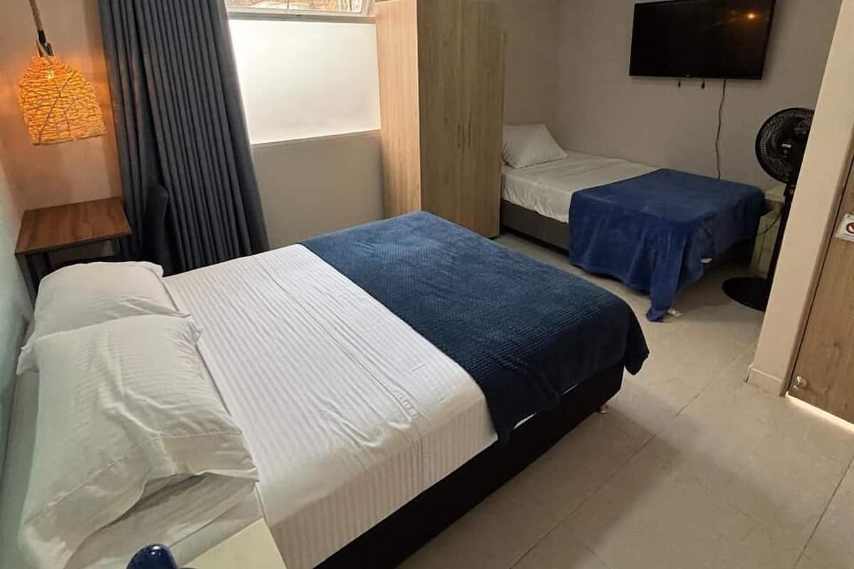 A hotel room with two beds, a TV, a desk with a lamp, and a window with curtains.