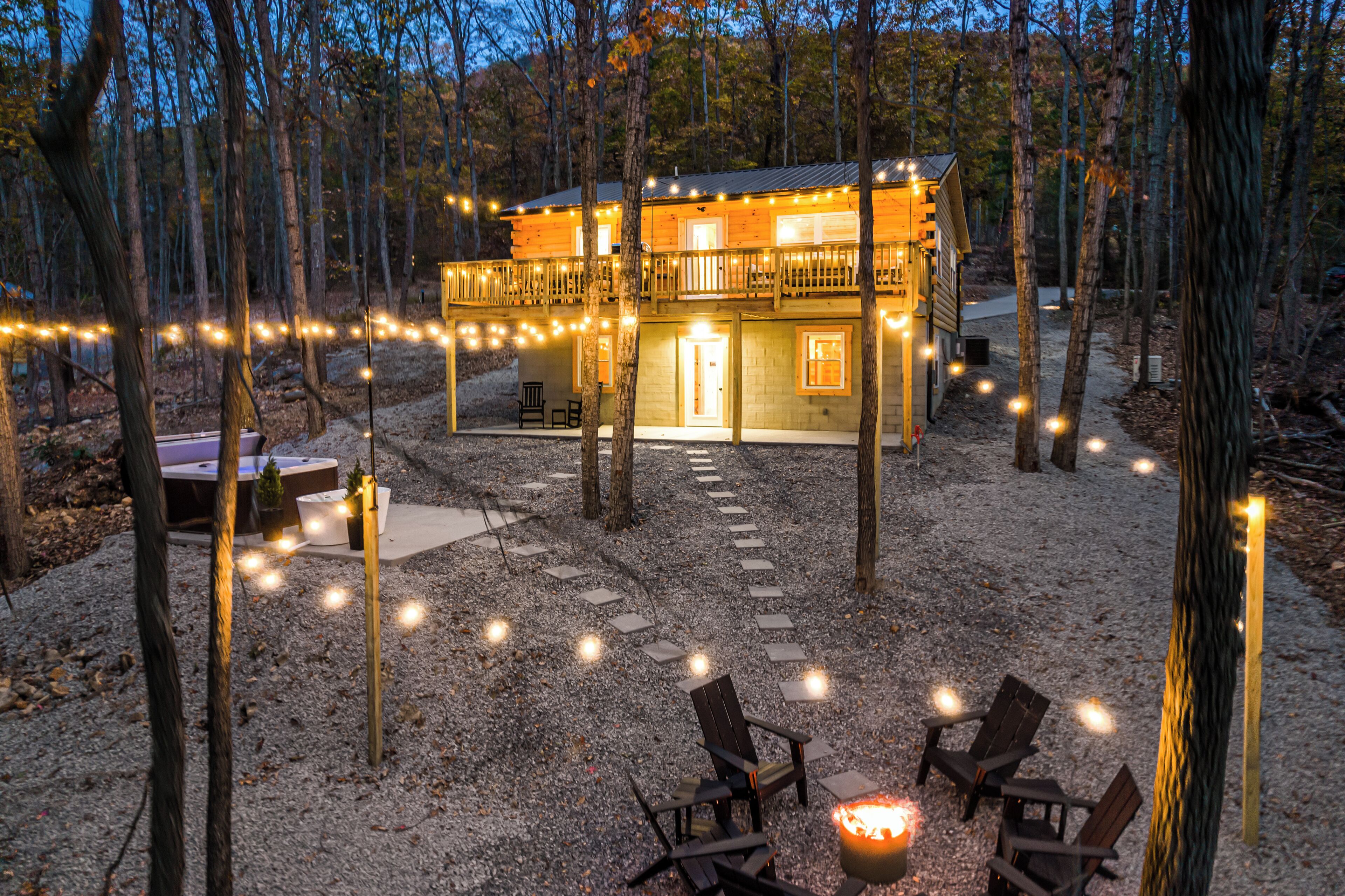 Een chalet met terras, omgeven door bomen, en buitenmeubels met lichtslingers.