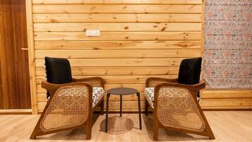 Interior de uma cabana de madeira com duas cadeiras de vime, uma mesa redonda pequena e uma parede de madeira com uma tomada.