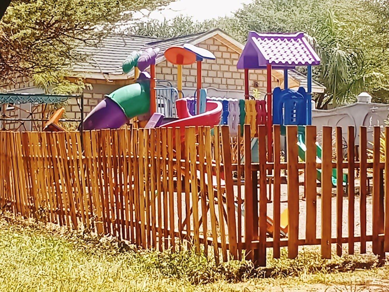 Una valla de madera frente a un parque infantil con un tobogán y estructuras para escalar.