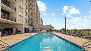 Une piscine avec des chaises longues, un espace abrité et un bâtiment doté de balcons.