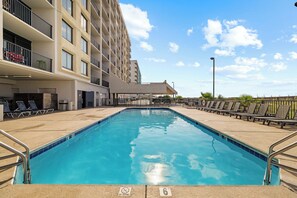 A swimming pool with lounge chairs, a covered area, and a building with balconies. - Island Winds West 670 by Liquid Life (Gulf Shores)