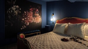Ein Schlafzimmer mit einem großen Blumenbild, einem Bett mit weißer Bettwäsche, einem roten Kopfteil und einem Nachttisch mit einer Lampe.
