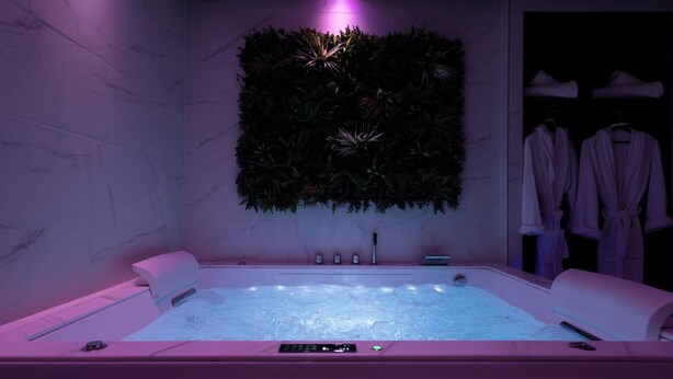 Ein moderner Wellnessraum mit einer großen Badewanne, einer Wandpflanze und einem Bademantelständer.
