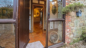 A wooden-framed door leading into a room with a tiled floor and a stone wall. - Upper Home Farm (Church Stretton)