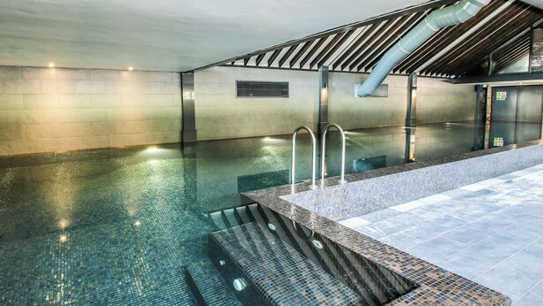 An indoor swimming pool with clear water, a tiled edge, and a metal handrail. - Upper Home Farm (Church Stretton)