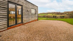 A rustic building with large windows and a gravel driveway leading to a green field. - Upper Home Farm (Church Stretton)