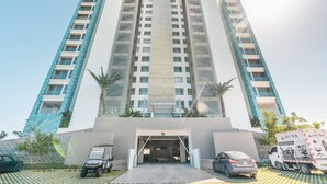 A high-rise building with a central entrance, multiple balconies, and a parking area with vehicles. - 7 Mares E2 in Punta Cana (Punta Cana)