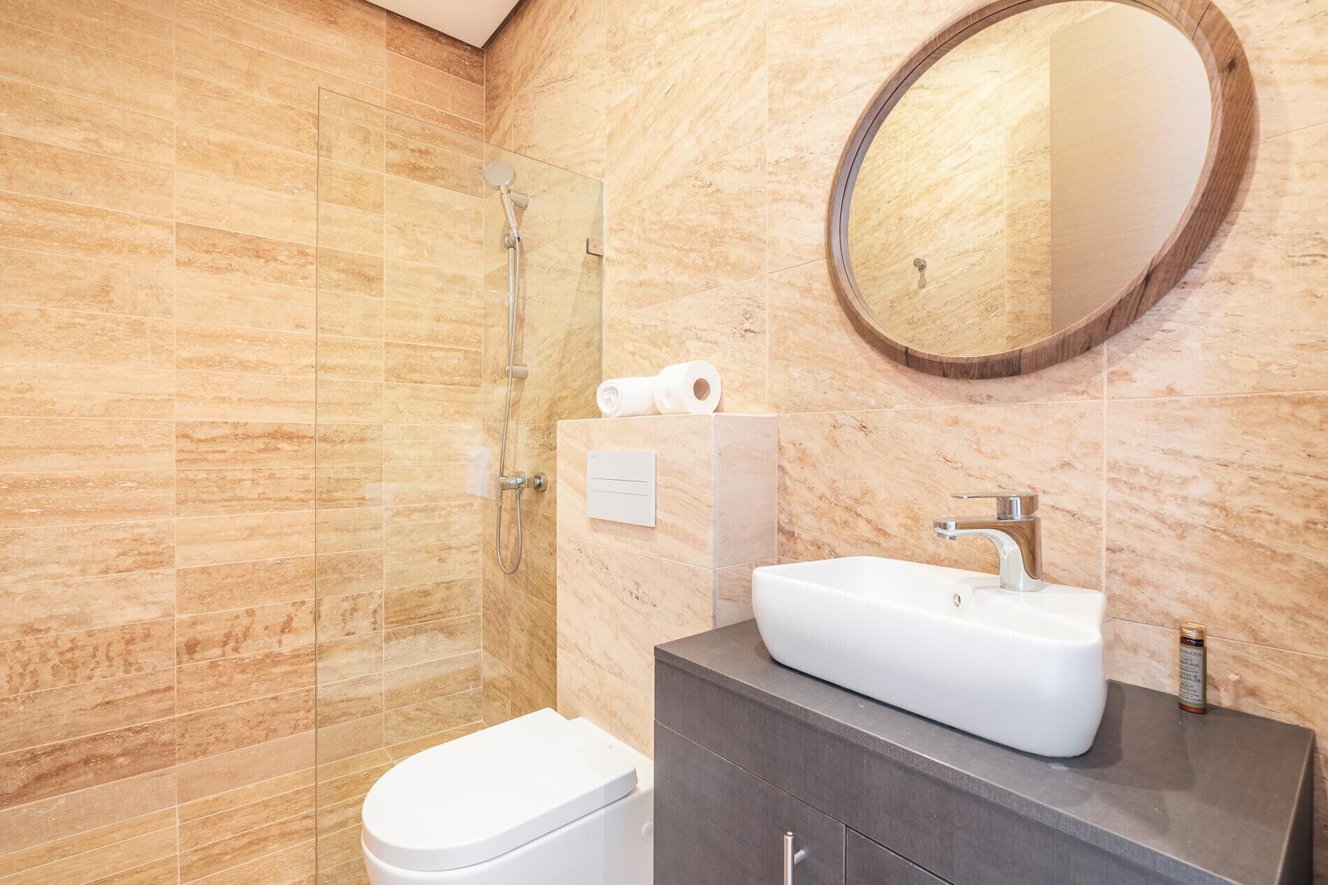 Een moderne badkamer met een douchecabine van glas, een wit toilet, een wastafelmeubel met een wastafel en een ronde spiegel.