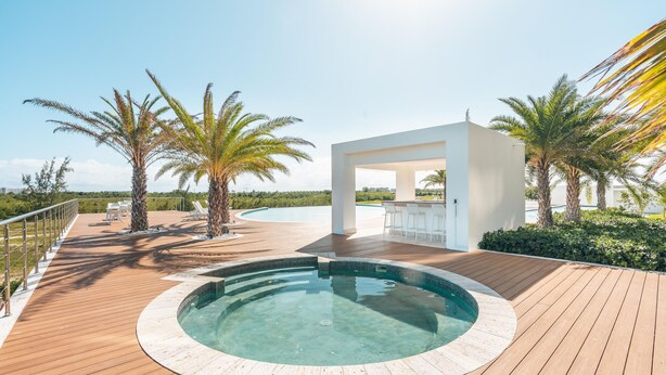 A modern outdoor pool area with a wooden deck, a hot tub, and a bar area surrounded by palm trees. - 7 Mares E2 in Punta Cana (Punta Cana)