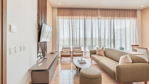 A modern living room with a sofa, ottoman, and chairs, a flat-screen TV mounted on the wall, and a large window with curtains. - 7 Mares E2 in Punta Cana (Punta Cana)