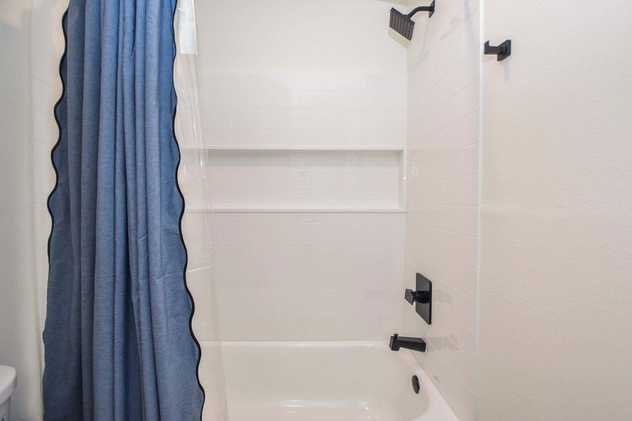 Une salle de bain avec des murs carrelés de carreaux blancs, une baignoire et une douche avec un rideau bleu.