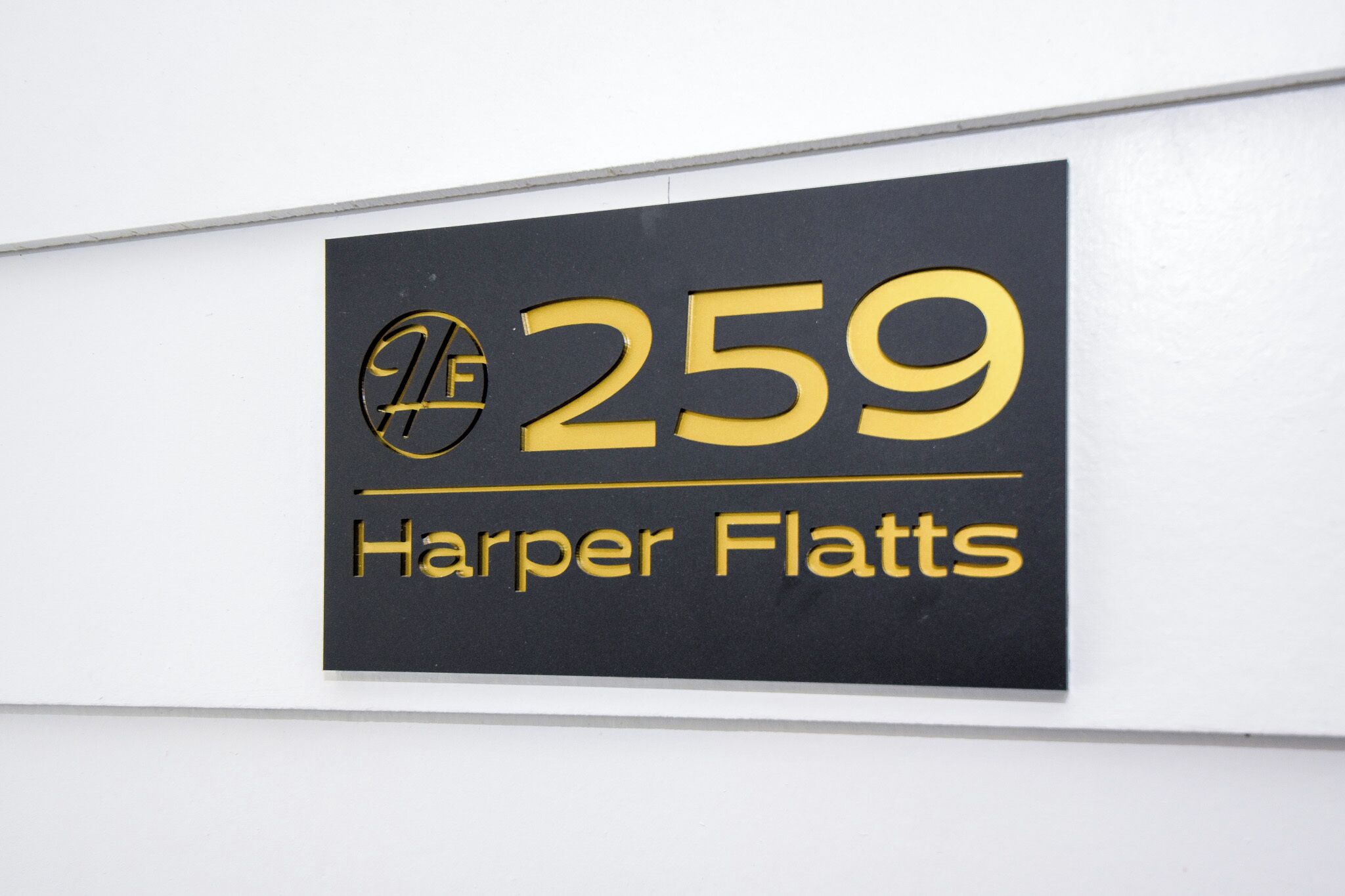 A sign with the number 259 and the name "Harper Flatts" on a white wall.