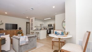A modern living room with a grey sofa, a round coffee table, and a TV. - New! Shug's Station, 2 BR, 2BA condo close to Auburn University, sleeps 4! (Auburn)