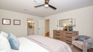 A bedroom with a bed, a dresser, a chair, a ceiling fan, and a mirror. - New! Shug's Station, 2 BR, 2BA condo close to Auburn University, sleeps 4! (Auburn)