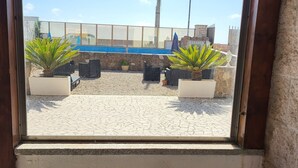 A window view of a patio area with potted plants, a stone wall, and a blue pool. - ALBACHIARA GUEST HOUSE (Fiumicino)