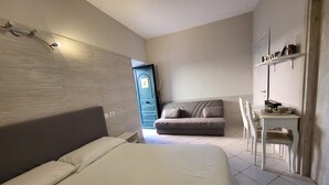 A hotel room with a bed, a sofa, a desk with a chair, and a wardrobe. - ALBACHIARA GUEST HOUSE (Fiumicino)