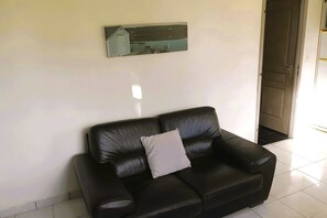 A black leather sofa with a cushion, a wall-mounted picture, and a door leading to another room. - Well-Decorated Rosemont Cottage in Prime Location (Saint-Pol sur Ternoise)