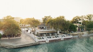A waterfront property with a covered patio, lounge chairs, and a boat dock. - Beau Rivage Suites (Aigialeia)