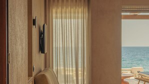 A modern room with a sofa, a flat-screen TV, and a view of the ocean. - Beau Rivage Suites (Aigialeia)
