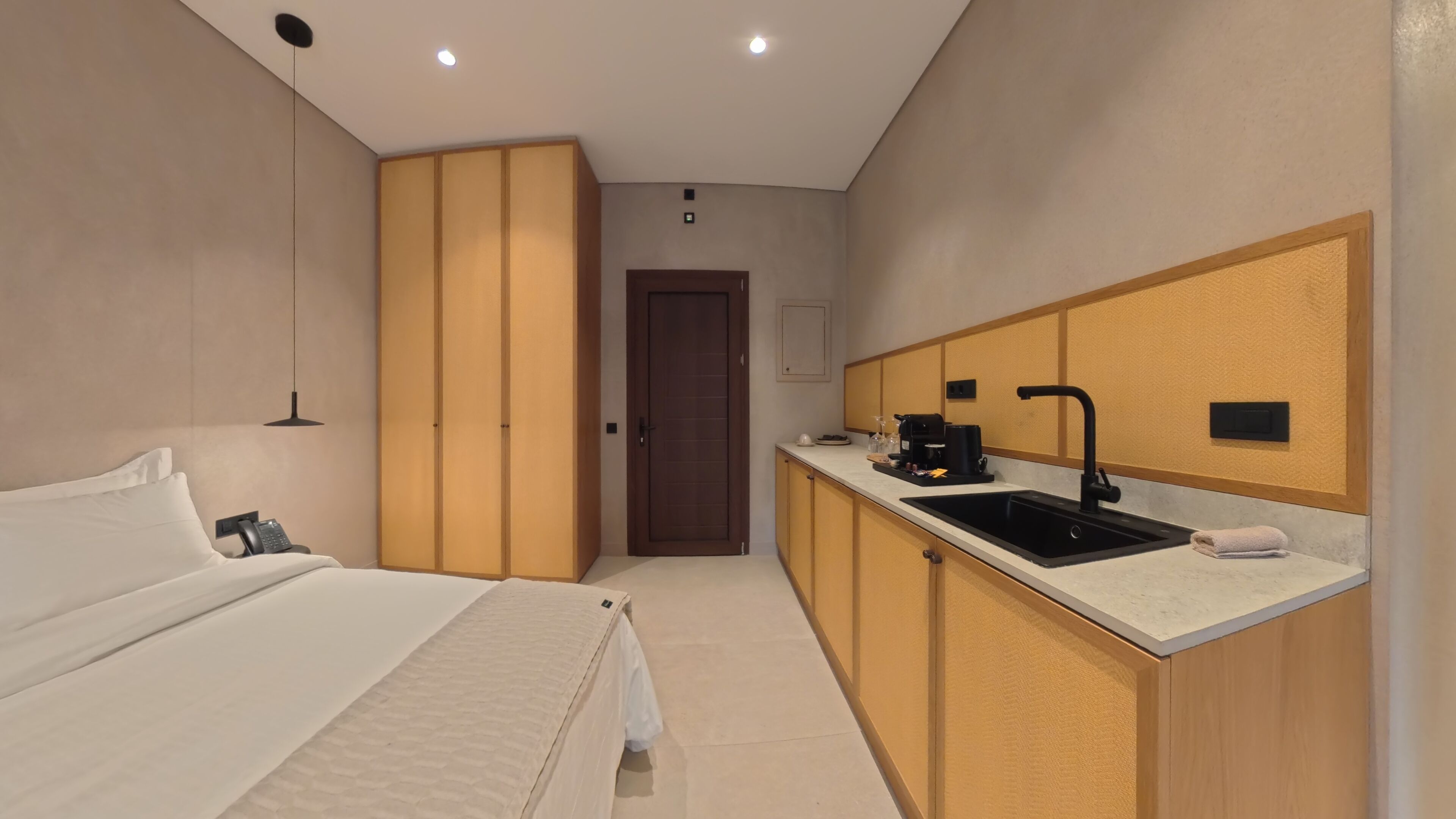 A hotel room with a bed, bedside telephone, a desk with a computer, a sink, and a wardrobe.