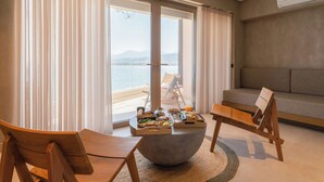 A room with a large window, a dining table with food, two wooden chairs, and a sofa. - Beau Rivage Suites (Aigialeia)