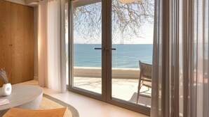 A modern room with a large sliding glass door leading to a balcony with a view of the sea. - Beau Rivage Suites (Aigialeia)