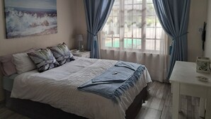 A bedroom with a bed, a nightstand, a lamp, a window with curtains, and a painting on the wall. - Cozy, quiet 1-bedroom pet-friendly cottage in the equestrian heart of the metro. (Midrand)