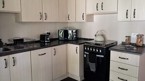 A modern kitchen with light wood cabinets, a black countertop, a gas stove, a kettle, and a toaster. - Cozy, quiet 1-bedroom pet-friendly cottage in the equestrian heart of the metro. (Midrand)