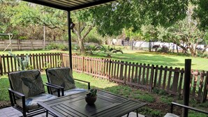 A patio with a table and chairs, surrounded by a wooden fence and a grassy yard. - Cozy, quiet 1-bedroom pet-friendly cottage in the equestrian heart of the metro. (Midrand)