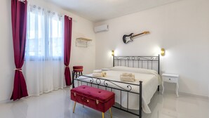 Ein Schlafzimmer mit Bett, einer Bank, einer Gitarre, einem Nachttisch und einem an der Wand befestigten Regal.