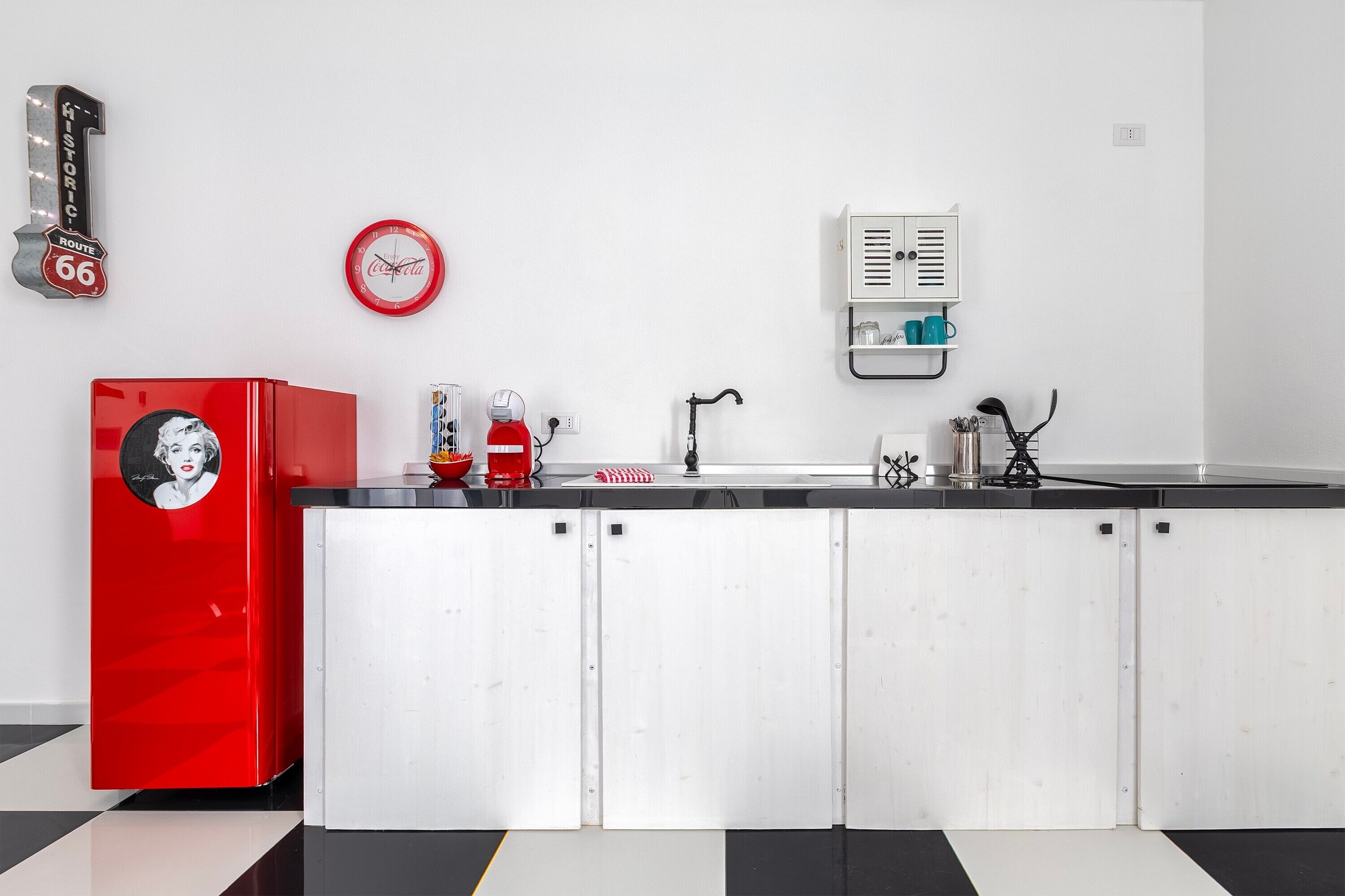 Una cocina con un refrigerador rojo, un reloj y un armario blanco.