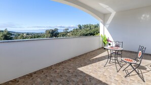 Ein Balkon mit gefliestem Boden, einem Tisch mit Stühlen und Blick auf die Landschaft.