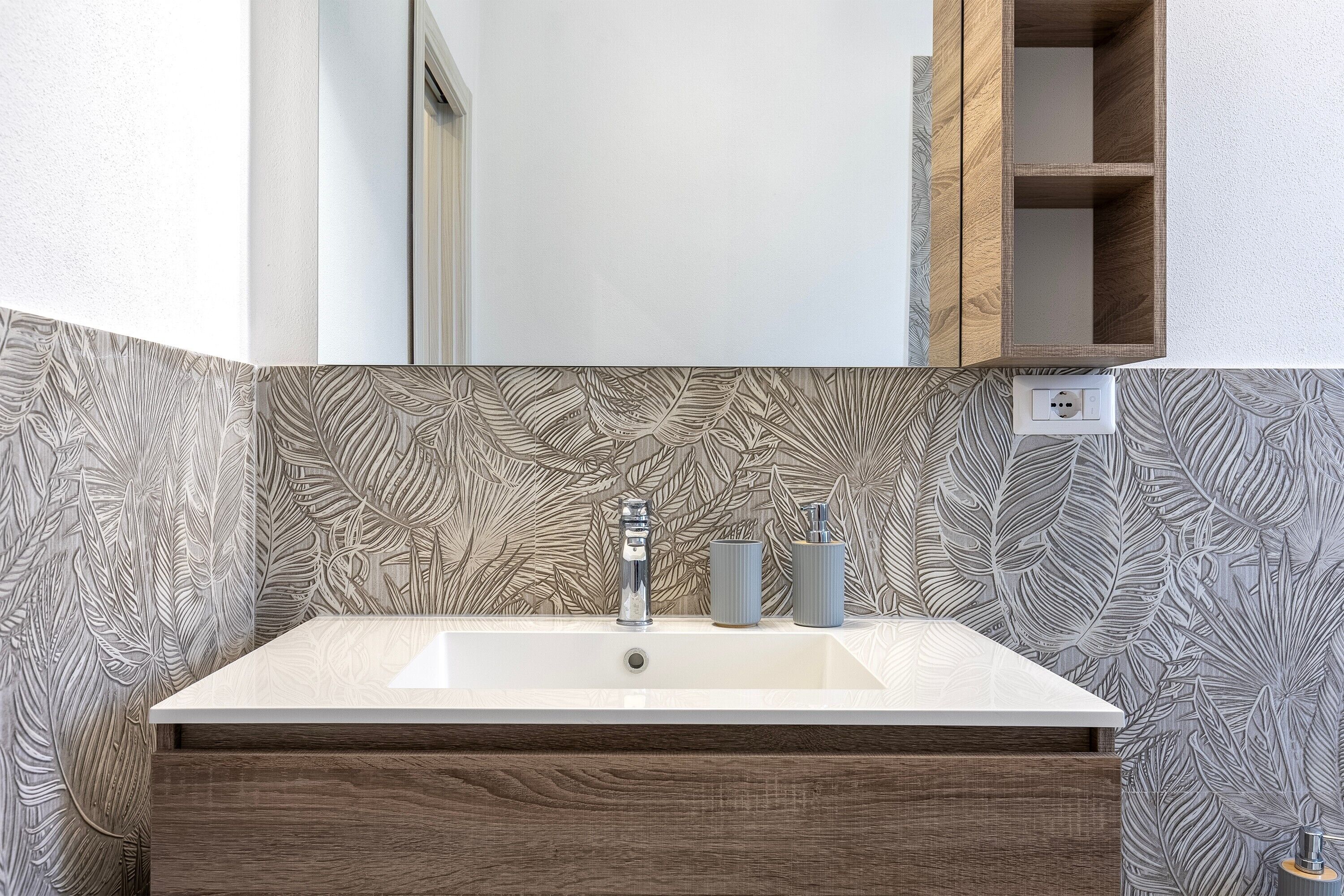 A bathroom with a white sink, wooden vanity, and a mirror above it.