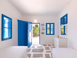 Une chambre avec deux lits, une commode blanche et une porte bleue donnant sur un espace extérieur.