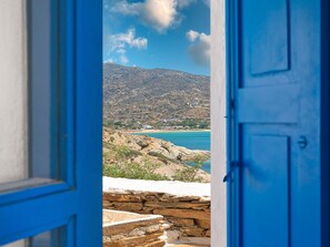 A view through a blue door to a coastal landscape with a stone wall, buildings, and a mountain. - Artistic Villa Hideaway (Ios)