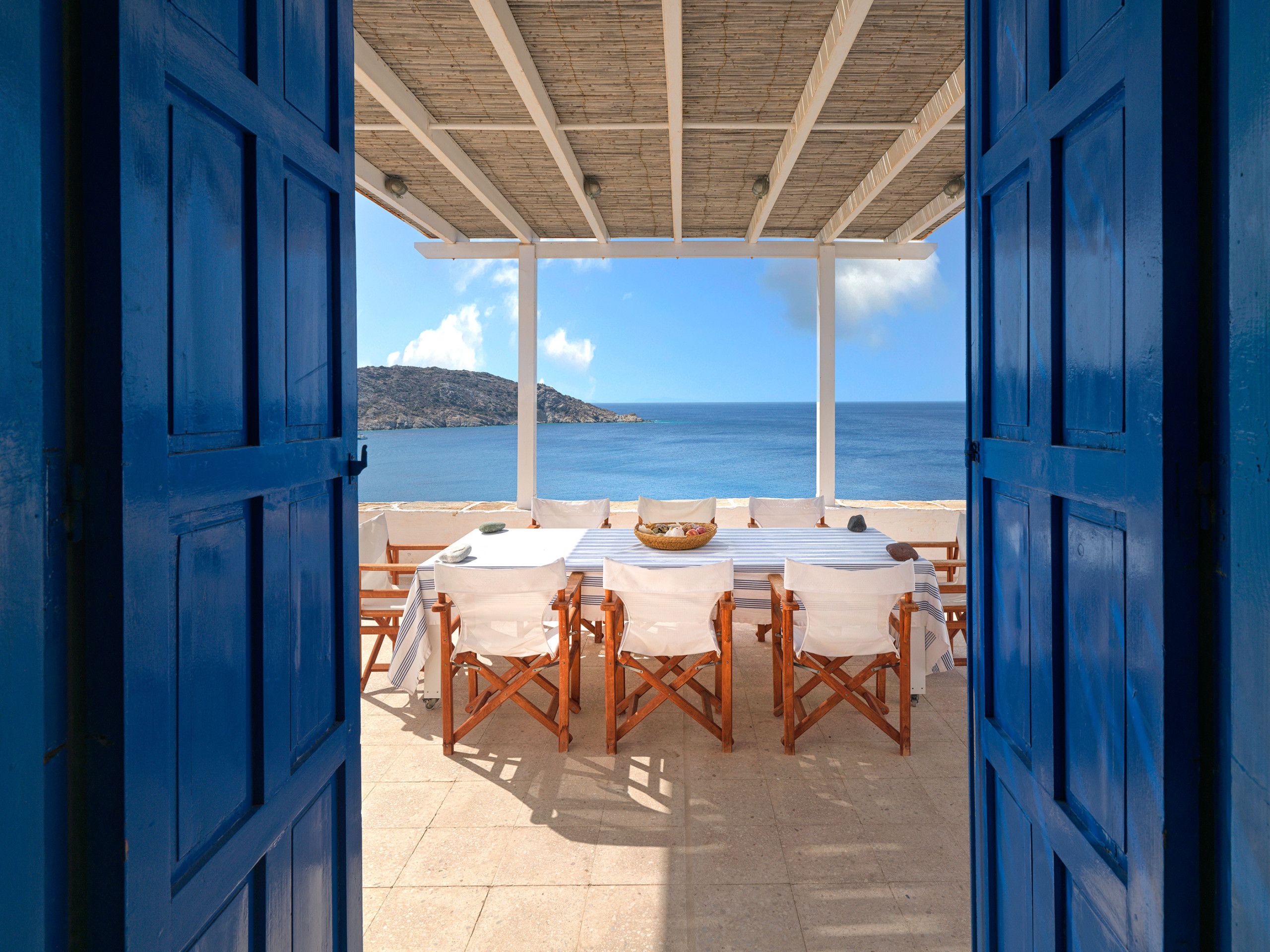 An open-air dining area with tables and chairs, overlooking a scenic view of the sea and a distant island.