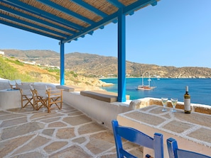 A terrace with stone flooring, blue chairs, and a table with a bottle and glasses. - Artistic Villa Hideaway (Ios)