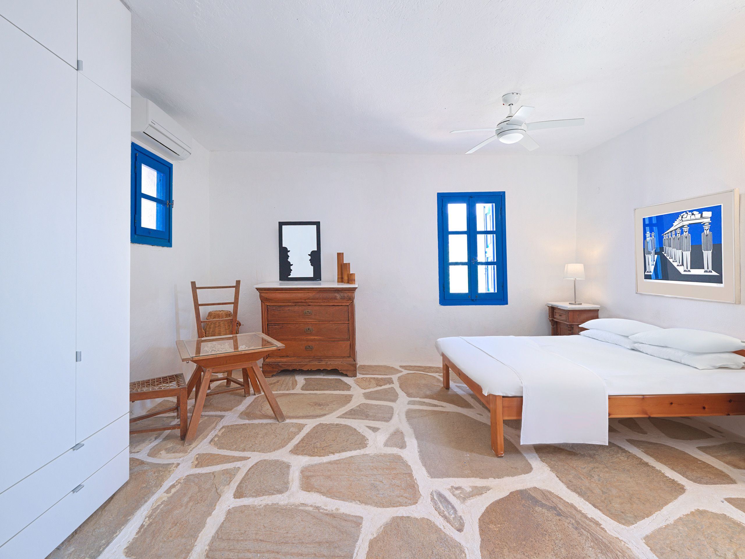 A bedroom with a bed, a dresser, a chair, a ceiling fan, and a stone-patterned floor.