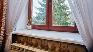 A window with white curtains, a wooden frame, and a small shelf with a bottle and reed diffuser. - Dwór Hetman w Jarosławiu (Jarosław)