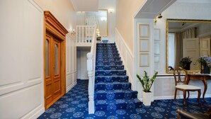 A grand staircase with blue carpet and wooden railings leading to an upper floor. - Dwór Hetman w Jarosławiu (Jarosław)