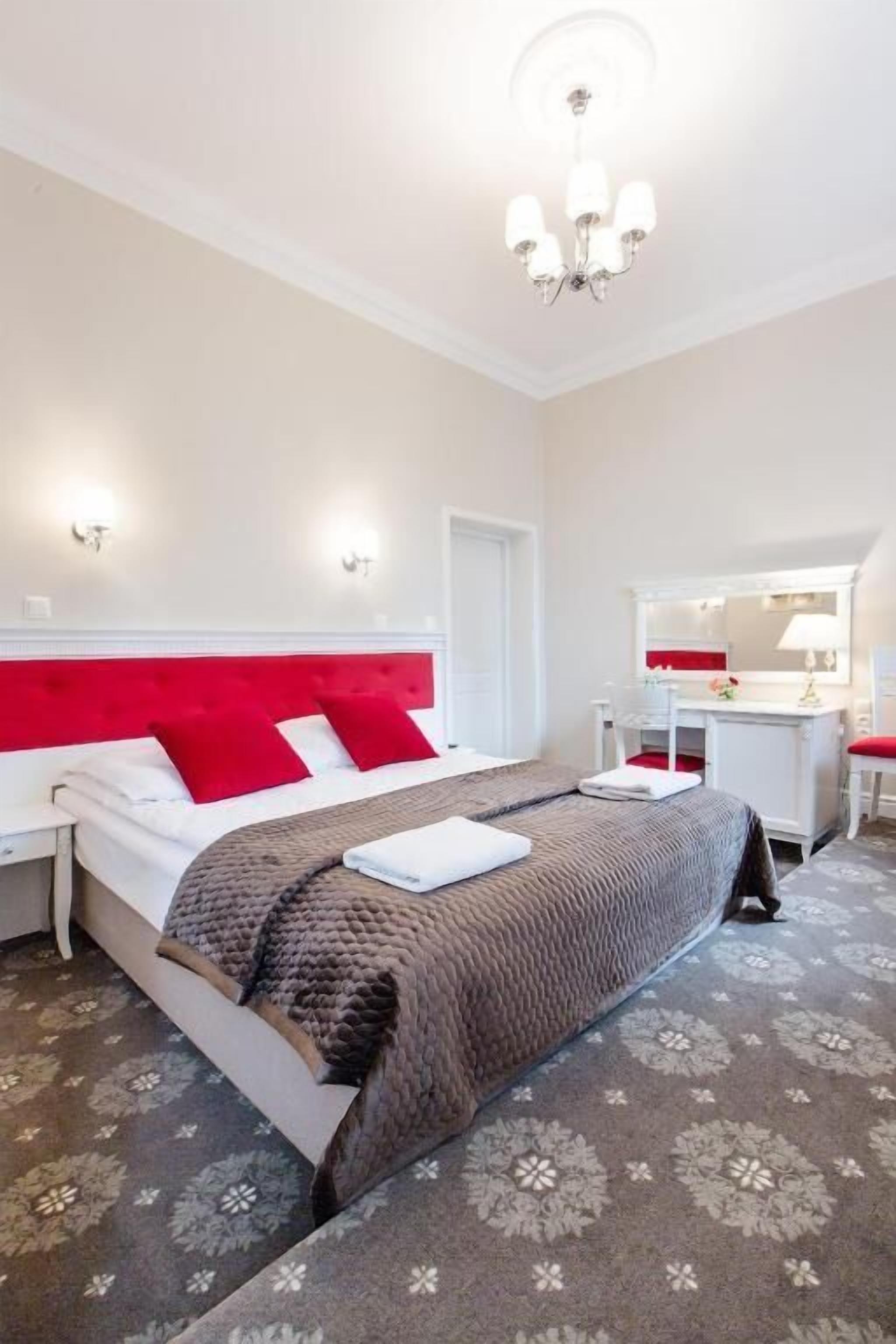 Habitación de hotel con cama, escritorio, silla, espejo y candelabro.