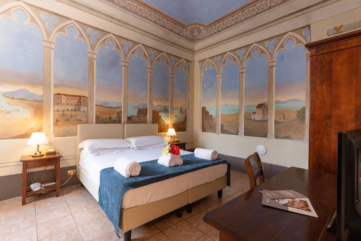 Una habitación de hotel con cama, mesitas de noche, televisor y mesa de comedor.