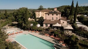 A large swimming pool surrounded by lounge chairs and umbrellas, with a building in the background. - Hotel with swimming pool in Riparbella (Riparbella)