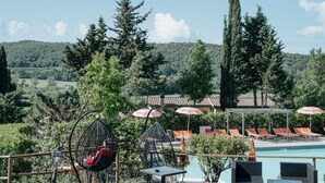 A poolside area with lounge chairs and umbrellas, surrounded by trees and a view of a forested hill. - Hotel with swimming pool in Riparbella (Riparbella)