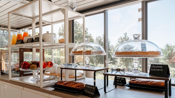A breakfast buffet with various food items and a view of trees through large windows. - Hotel with swimming pool in Riparbella (Riparbella)